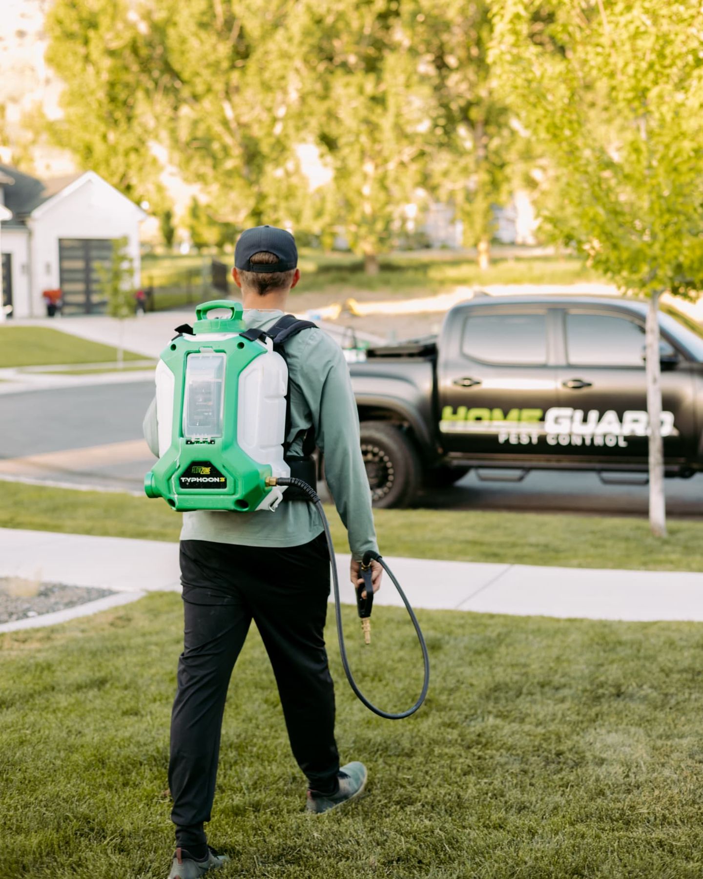 HomeGuard Pest Control technician treating the exterior of a Cache Valley home with a backpack sprayer